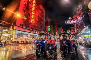 A row of tuktuk is waiting for passengers udnerneath the city's neon signs