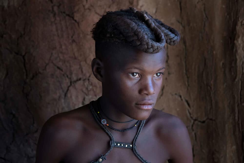 Into the wild Namibia - A himba girl is portrayed in her family's clay house where soft daylight is coming in from the doorway