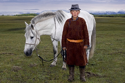 Mongolian boy with hat standing in front of a white horse